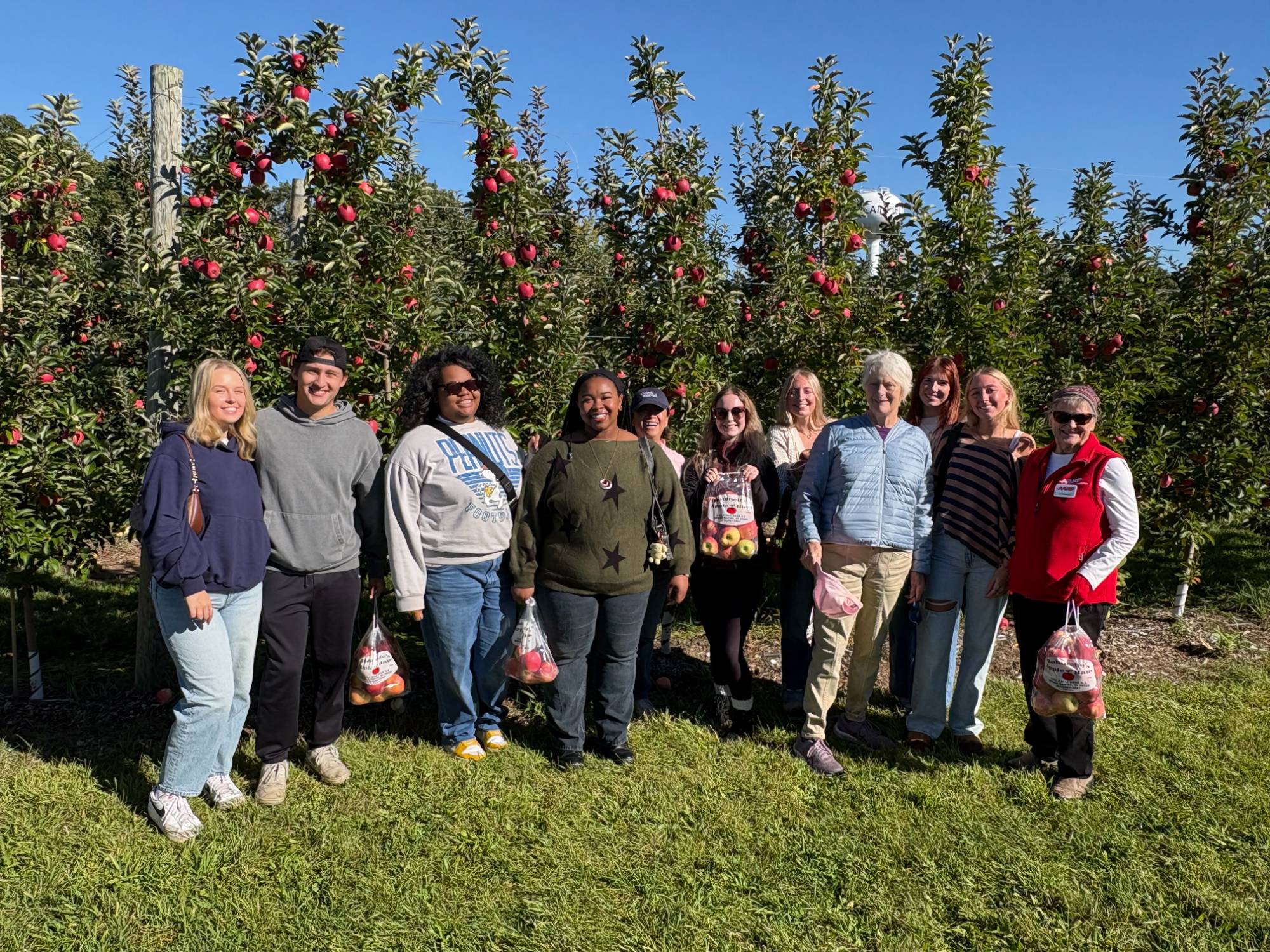 SAGE and Grand Connection members smiling for a picture in front of orchard